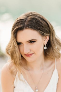 Beyaz elbiseli güzel bir kızın portresi. Arka planda saçı ve makyajı var.