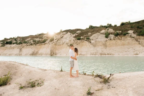 A beautiful young couple in love, a man and a woman embrace, kiss near a blue lake and sand at sunset. Vacation at the sea on the beach, sunset, morning, honeymoon, tropics, ocean, girl, relationship.
