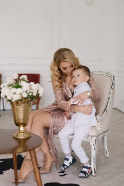 Güzel anne ve oğul kucaklaşıp evde şık kıyafetler giyip oynuyorlar.