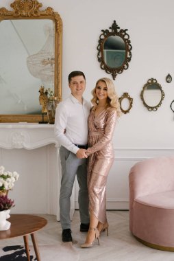 Güzel bir erkek ve kadın zarif giysiler içinde evin güzel bir köşesinde kucaklaşırlar.