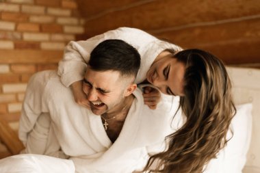 Genç, güzel, mutlu, yeni evliler aşık bir adam ve bir kadın yatakta uzanıyor, gülümsüyor ve evde sarılıyorlar.