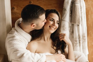 Genç, güzel, mutlu, yeni evliler aşık bir adam ve bir kadın yatakta uzanıyor, gülümsüyor ve evde sarılıyorlar.