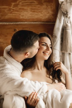 Genç, güzel, mutlu, yeni evliler aşık bir adam ve bir kadın yatakta uzanıyor, gülümsüyor ve evde sarılıyorlar.