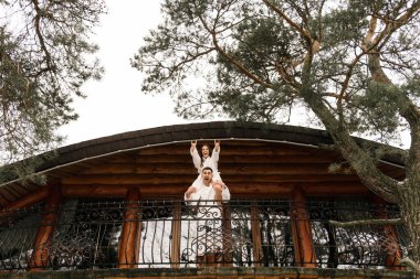 Genç, güzel, mutlu, yeni evliler. Beyaz banyo cüppeli bir adamla bir kadın evin balkonunda gülümsüyor ve sarılıyorlar.