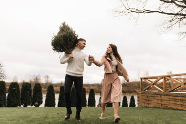 Genç ve güzel mutlu aşıklar, kışın yaşayan bir Noel ağacı ellerinde nehir kıyısının arka planında aşk hikayesi.