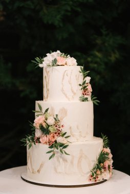 Lüks düğün, çiçeklerle süslenmiş beyaz pasta, arka planda gece çekilmiş fotoğraf.