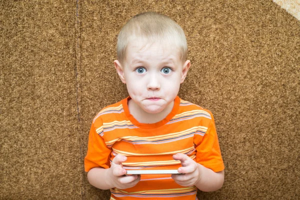 Surprised boy holding a smartphone in the hands and sitting on the couch — Stock Photo, Image
