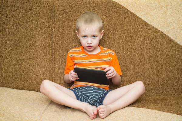 Liten pojke spelar i plattan på soffan och titta på den — Stockfoto
