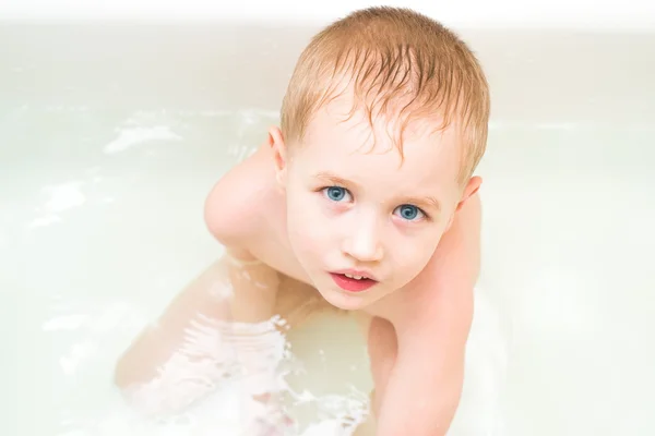 En liten gutt sitter på badet og ser inn i kameraet. – stockfoto
