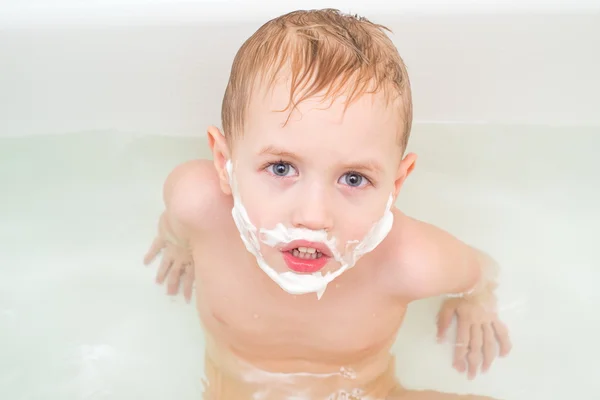 Маленький мальчик в ванной с усами и бородой из пены — стоковое фото