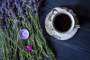 Koyu mavi ahşap arka planda bir fincan kahve ve lavanta çiçeği..