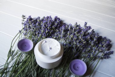 Beyaz ahşap arka planda lavanta çiçekleri, mumlar ve krema. Güzellik bakımı.