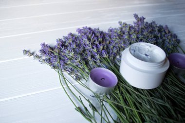 Beyaz ahşap arka planda lavanta çiçekleri, mumlar ve krema. Güzellik bakımı.