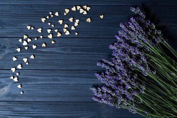 Lavender flowers and wooden love hearts on a dark blue wooden table. Beautiful romantic background with copy space.