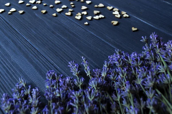 Lavender flowers and wooden love hearts on a dark blue wooden table. Beautiful romantic background with copy space.