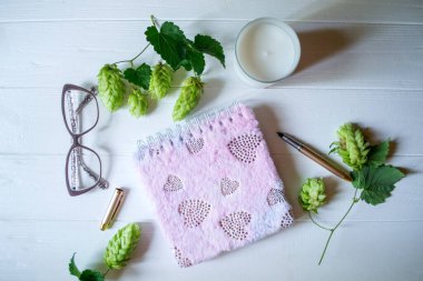 Açılmış not defteri, kalem, beyaz mum, beyaz ahşap bir masa üzerindeki süs olarak hoplama kadehleri ve dalları. Metin için alanı olan masaüstü natürmortu.