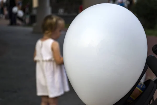 White balloon close-up and children playing in the background.