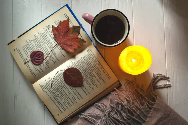 A cup of tea near book and wollen blanket with decoration by fallen leaves. Cozy autumn.