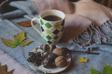 Mavi ahşap arka planda sonbahar yapraklarıyla süslenmiş bir fincan çay ve tatlı atıştırmalıklar. Mevsimlik durgun hayat.