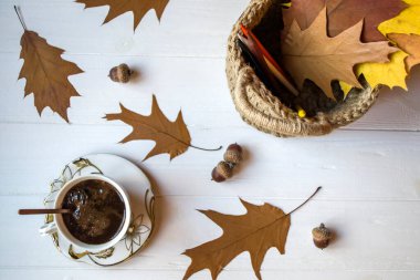 Beyaz ahşap bir masada bir fincan kahve ve meşe yapraklarıyla süsleme..