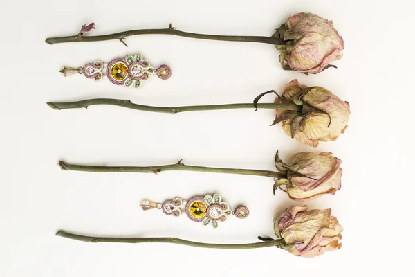 Soutache bijouterie brincos rosa com rosa amarelo e ciano cristais no fundo branco com flores secas Fotos De Bancos De Imagens