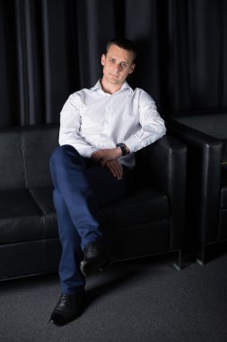 Genç adam koyu arka plan üzerinde gülümseyen koltuk poz