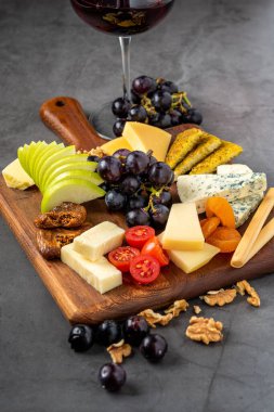 Kırmızı şarap ve ahşap tabakta meyveli çeşitli peynir tabağı.