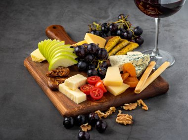 Kırmızı şarap ve ahşap tabakta meyveli çeşitli peynir tabağı.