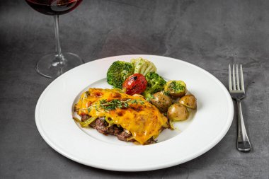 Çedar peynirli biftek, patates ve brokoli, koyu taştan arka planda.