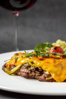 Çedar peynirli biftek, patates ve brokoli, koyu taştan arka planda.