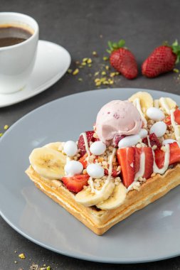 Çilekli ve muzlu Belçika waffleları ve bir fincan kahve.