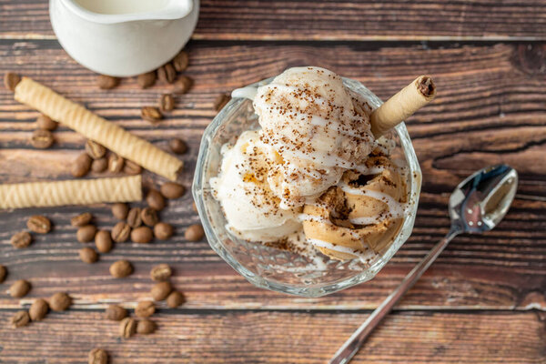 Walnut, cream and caramel Roma ice cream in a glass bowl with ground coffee and white chocolate sauce poured over it.