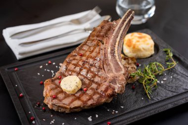 Siyah taş tabakta ızgara dana pirzola, sos ve garnitür..