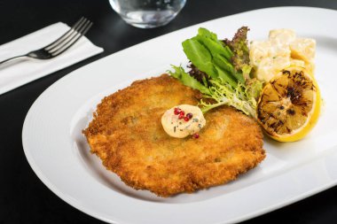 Beyaz porselen tabakta tereyağlı tavuk şnitzel ve patates salatası.