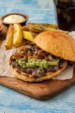 Çedar peynirli ve karamelli soğanlı ezme burger, patates kızartmasıyla servis edilir.