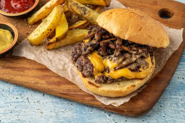 Çedar peynirli ve karamelli soğanlı ezme burger, patates kızartmasıyla servis edilir.