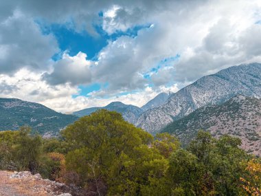Dramatic mountain landscape with cloudy sky and green forest foreground