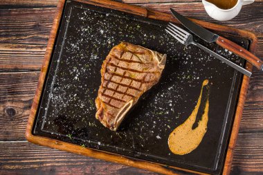 Lezzetli New York bifteği orta pişmiş ve siyah tabakta servis ediliyor.