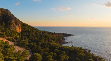 Çam ormanı üzerinde gün batımının ılık ışığı ve sakin Akdeniz kıyısı