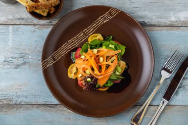 Kahverengi tabakta garnitürle servis edilen renkli sebze salatası.