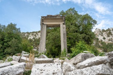 Antik Termessos şehrindeki Hadrian Geçidi 'nin kalıntıları ağaçlarla çevrili ve kayalık bir ön planda.
