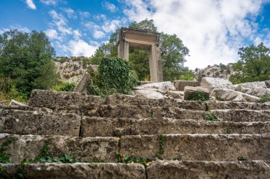 Antik Termessos şehrindeki Hadrian Geçidi 'nin kalıntıları ağaçlarla çevrili ve kayalık bir ön planda.