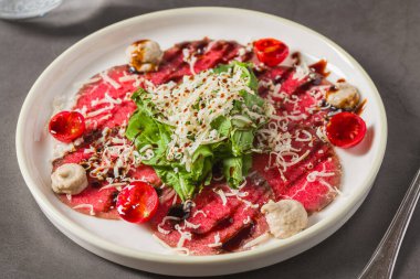 İnce dilimlenmiş et carpaccio, yeşillik, peynir ve vişneli domatesle servis edilir.