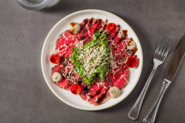 İnce dilimlenmiş et carpaccio, yeşillik, peynir ve vişneli domatesle servis edilir.