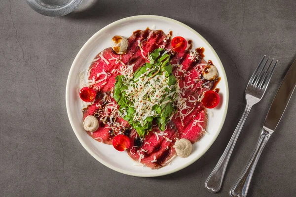 İnce dilimlenmiş et carpaccio, yeşillik, peynir ve vişneli domatesle servis edilir.