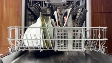 Adam temiz tabakları boşaltıyor ve kirli eşyaları bulaşık makinesine yüklüyor.