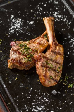 Siyah taş tabakta servis edilen ızgara kuzu pirzolası.