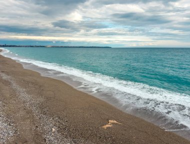 Çakıl taşı kumsalının geniş açılı manzarası ve bulutların altında turkuaz deniz