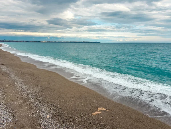 Çakıl taşı kumsalının geniş açılı manzarası ve bulutların altında turkuaz deniz