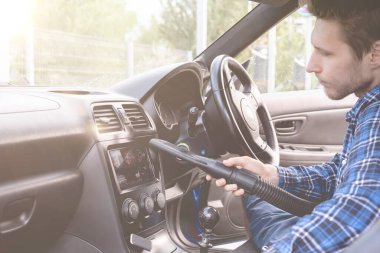 Erkek kişi arabanın içini elektrikli süpürgeyle temizliyor.